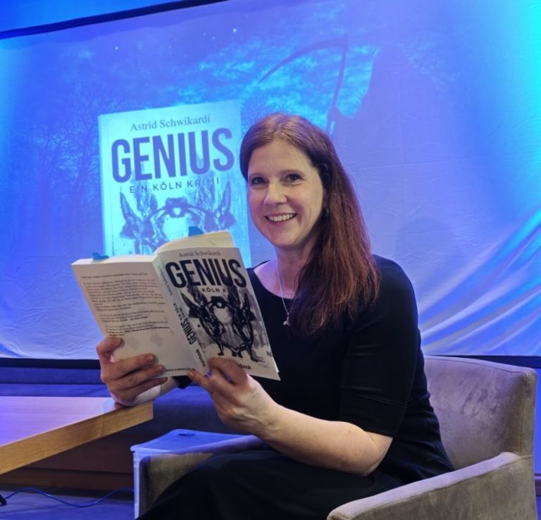 Frau mit einem Buch "Genius" in der Hand, lächelnd vor einer blauen Hintergrundleinwand.