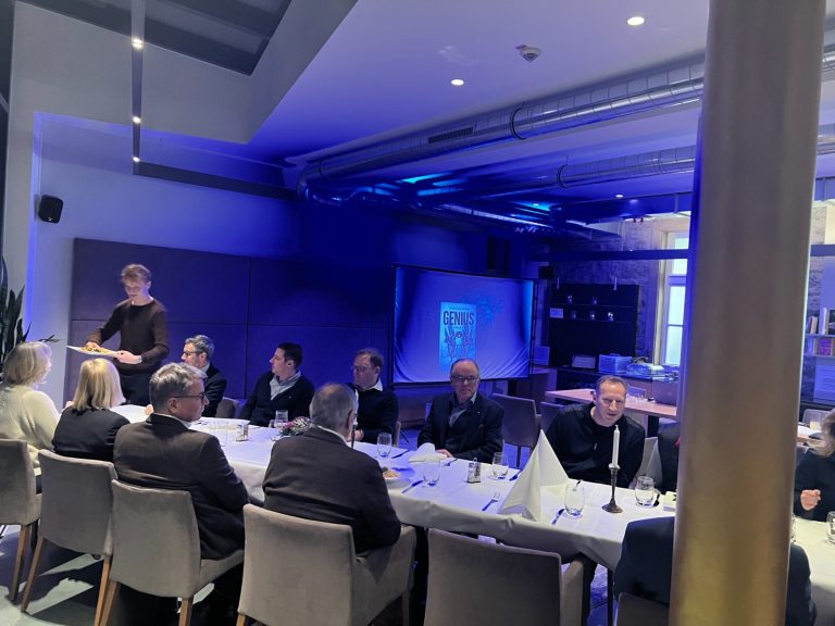 Einblicke in die Krimilesung - Eine Gruppe von Menschen sitzt an einem langen Tisch in einem modernen Raum mit blauer Beleuchtung.