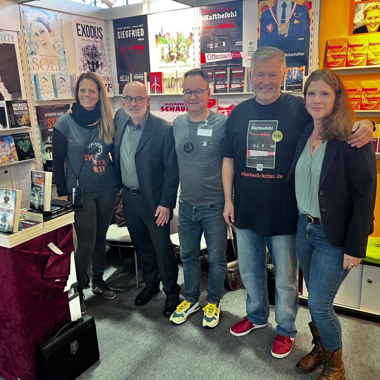 Gruppe von fünf Personen lächelnd auf einer Messe, umgeben von Ausstellungsständen.