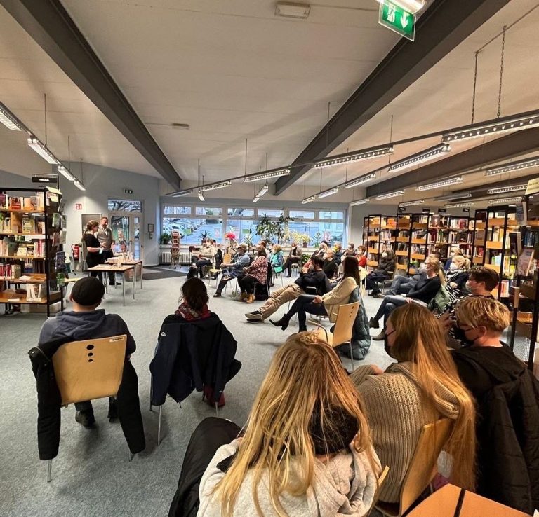 Lesung in einer Buchhandlung mit Publikumsanordnung und vielen Bücherregalen.
