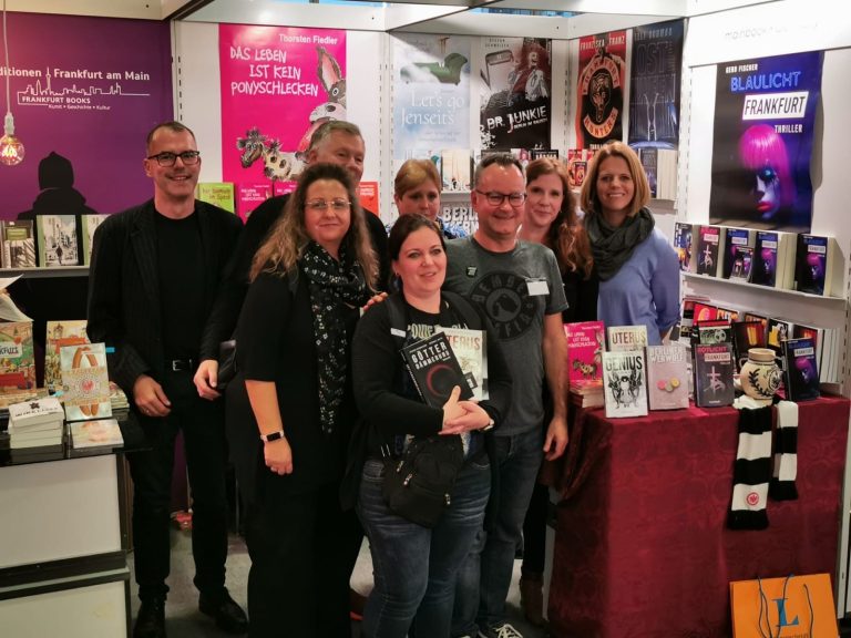 Gruppe von Menschen steht vor einem Bücherstand auf einer Messe.