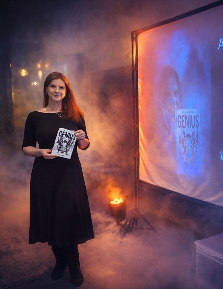 Frauen in einem schwarzen Kleid hält das Buch Genius - Ein Köln Krimi, hinter ihr ein leuchtendes Plakat.
