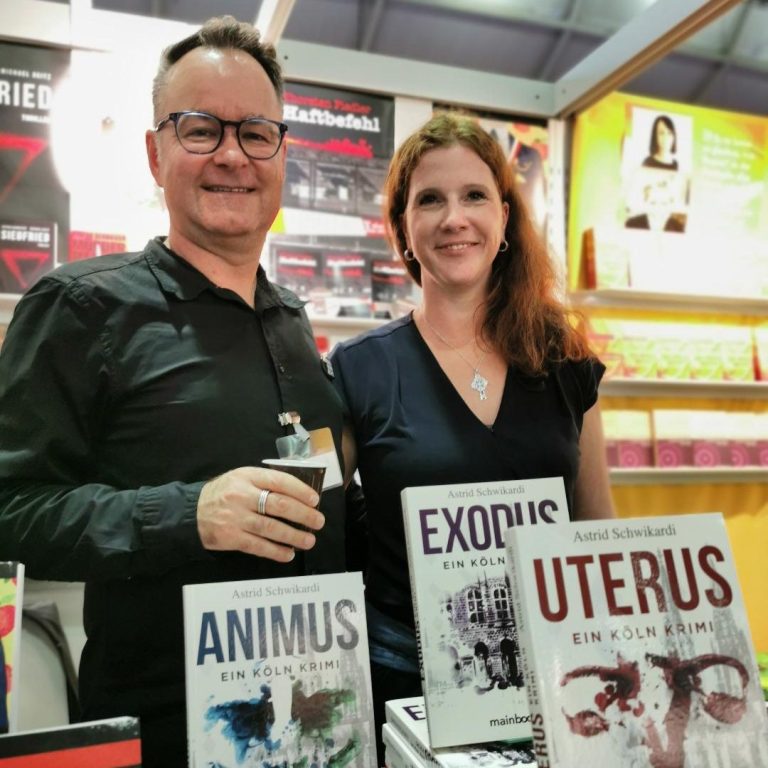 Ein Mann und eine Frau stehen lächelnd hinter den Kriminalromanen Uterus, Animus und Exodus von Astrid Schwikardi