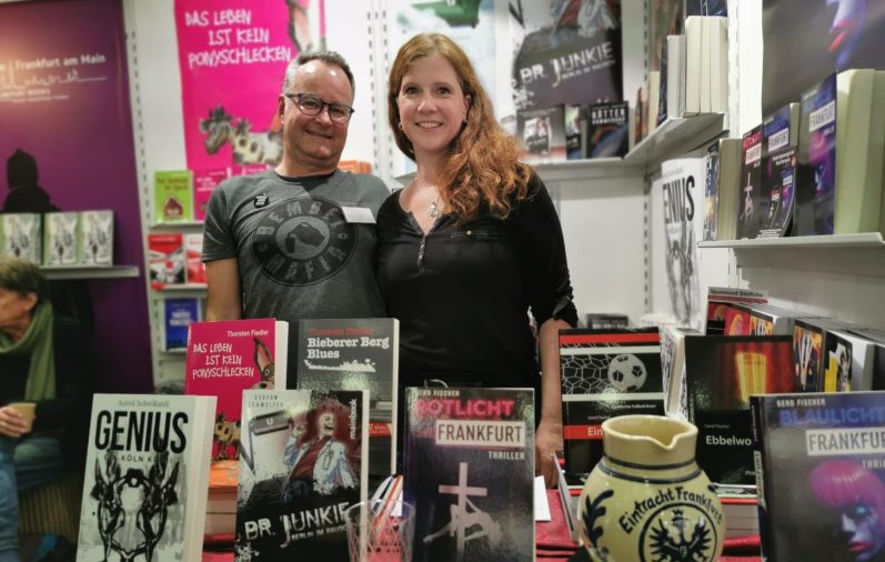 Zwei Personen stehen an einem Büchertisch mit verschiedenen ausgestellten Büchern - Astrid Schwikardi und Gerd Fischer von mainbook.