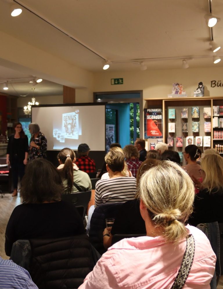 Vortragssituation in einem Buchladen mit Publikum und Projektor im Hintergrund.