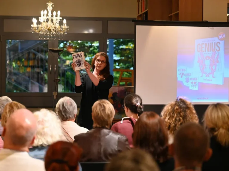 Frau, Astrid Schwikardi, präsentiert ihr Buch Exodus vor einem Publikum in einem beleuchteten Raum.