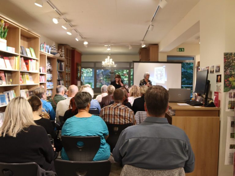 Veranstaltung in einem Buchladen mit Publikum, Podium und Präsentation im Hintergrund.
