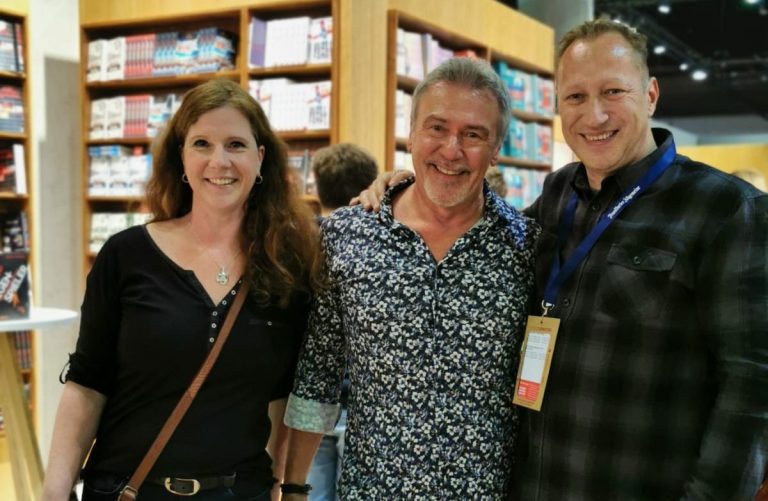 Drei Personen stehen lächelnd vor einem Bücherregal.